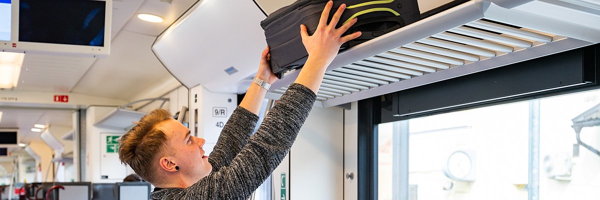 A passenger is loading a suitcase on the luggage rack on the train