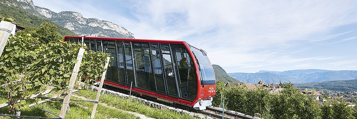 Cabina della funicolare della Mendola, vista dal lato, leggermente coperta dalla vegetazione.