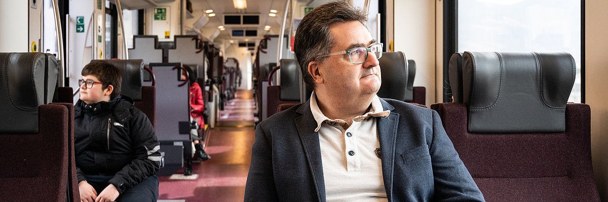  A passenger with a smartphone in one hand is looking outside the train window.