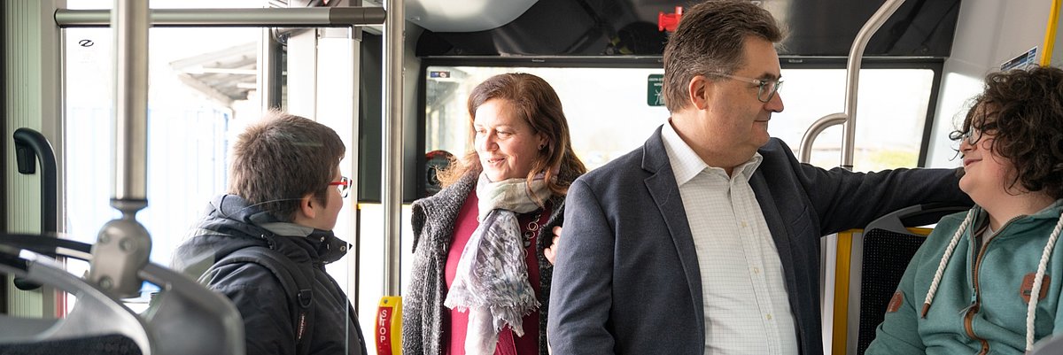 4 passengers, 2 adults and 2 young people, are talking to each other on the bus. One of them is sitting.