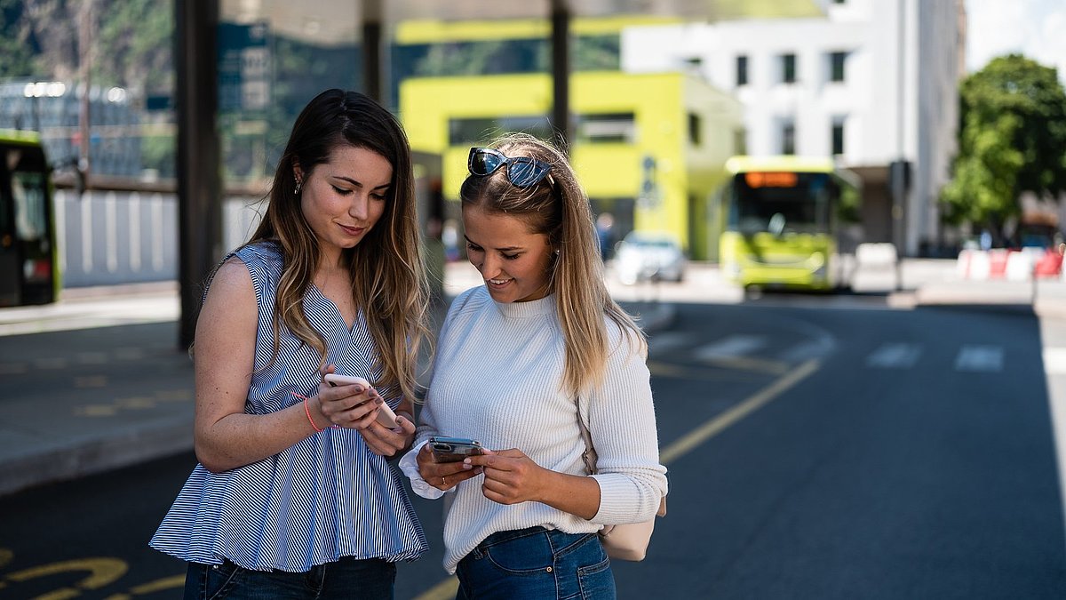 Two girls with smartphones at the Bolzano bus station